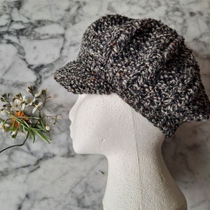 K&ouml;nnte beinhalten: Eine schwarze und wei&szlig;e Tweed-Newsboy-M&uuml;tze mit leicht eingefallener Krone. Die M&uuml;tze sitzt auf einem wei&szlig;en Mannequin-Kopf.