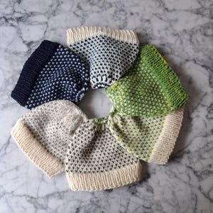 May include: Five knitted hats in a circle, featuring different color combinations and patterns. The hats are made with a textured stitch and have a folded brim. The colors include navy blue, white, green, and beige.