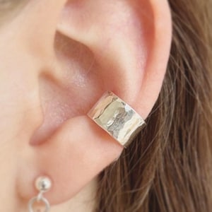 May include: Silver ear cuff with a hammered texture. The cuff is worn on the upper part of the ear.