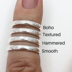 May include: Four silver rings stacked on a finger, showing different finishes: boho, textured, hammered, and smooth.