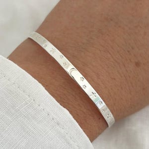 May include: A silver bangle bracelet with a repeating pattern of stars and moons.