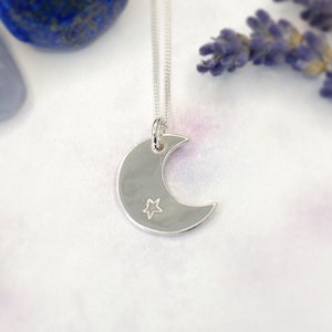 May include: A silver crescent moon necklace with a small star etched into the surface.