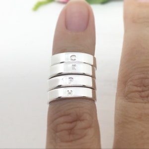 May include: A set of five silver rings stacked on a finger. Each ring has a different letter engraved on it: C, K, P, H.
