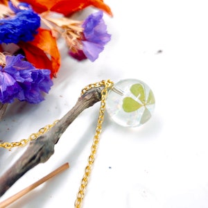 Women&#39;s necklace with sphere pendant, real flower, four-leaf clover, lucky charm, opal flakes in resin. Golden steel chain. Botanical jewellery.
