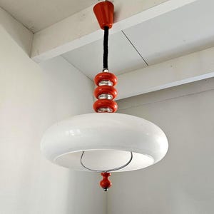 May include: A white, retro-style pendant light with a rounded, saucer-like shade. The light fixture features a series of three stacked, orange-red spheres and a matching top piece. A black cord suspends the light from the ceiling.