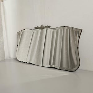 May include: A vintage Art Deco style mirror with a wavy, pleated design. The mirror has a silvered surface and a dark frame. A decorative silver metal accent is at the top center.