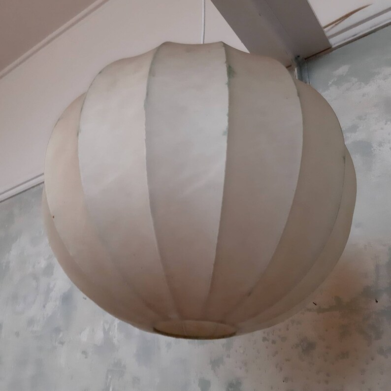 May include: A white, round, pleated lampshade hangs from the ceiling. The lampshade is made of a soft, fabric-like material and has a slightly textured surface.