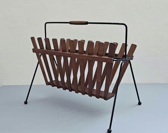 May include: A mid-century modern magazine rack with a black metal frame and wooden slats. The rack has a handle on the top and stands on four legs.