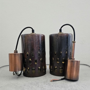 May include: Two copper pendant lights with a black wire and a cutout design. The lights have a distressed finish and a gold interior.