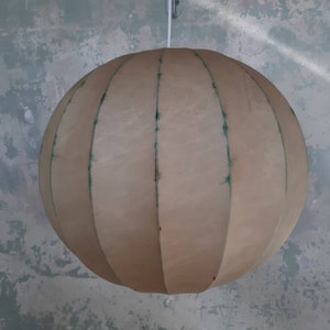 May include: A beige, round, fabric lampshade with vertical seams. The lampshade is suspended from a white cord.