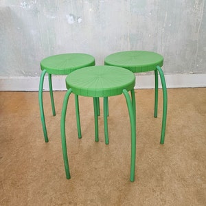 Puede incluir: Tres taburetes de plástico verde con un diseño de estrella en el asiento. Los taburetes tienen cuatro patas cada uno.