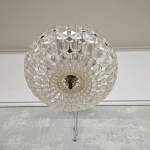 May include: A clear glass chandelier with a round, faceted design. The chandelier has a silver metal stem.