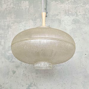 May include: A vintage, textured glass pendant light fixture. The light has a round, oval shape with a textured surface and a cream-colored wooden stem. The fixture is suspended from a metal bracket.