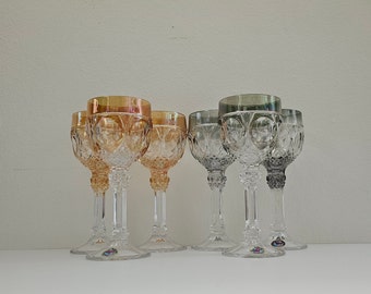 May include: Set of six clear glass stemmed drinking glasses with intricate cut designs. The glasses have a variety of colors, including clear, amber, and green.