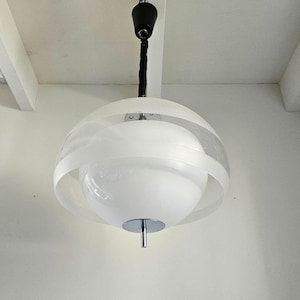 May include: A white, round, modern pendant light fixture with a chrome finish and a black cord.