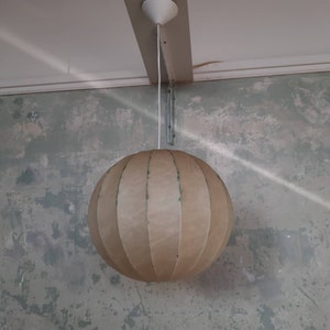 May include: A beige, round, hanging lampshade with vertical lines. The lampshade is made of a textured material and is hanging from a white cord.