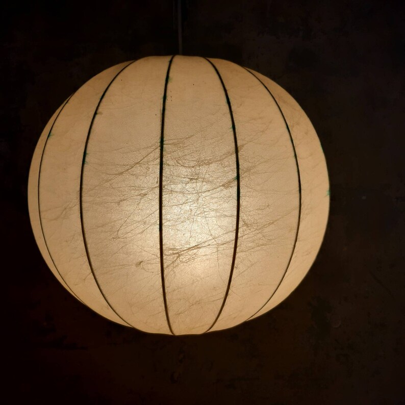 May include: A white, round, paper lampshade with vertical lines and a light shining through it.