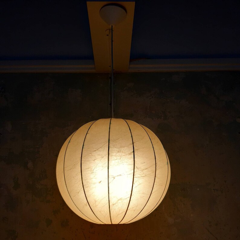 May include: A white, round, paper lampshade with a light inside, hanging from a ceiling.