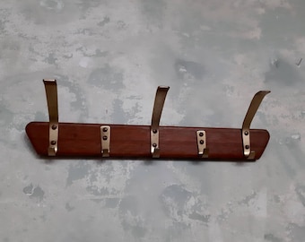 May include: A wooden coat rack with five gold metal hooks. The rack is made of dark wood and has a rectangular shape.
