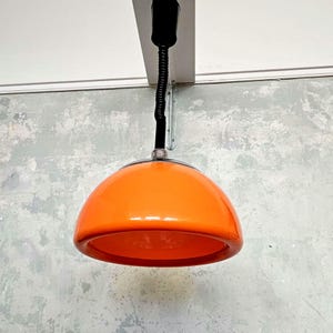 May include: A bright orange pendant light with a black cord and a metal ceiling mount.