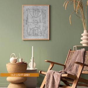 Op de afbeelding: Een ingelijste print van een basketbalveld diagram in lichtgrijs. Het gedetailleerde diagram bevat lijnen, cirkels en tekst, tegen een achtergrond met textuur. De lijst is gemaakt van lichtbruin hout. De print is getiteld "THE COURT".