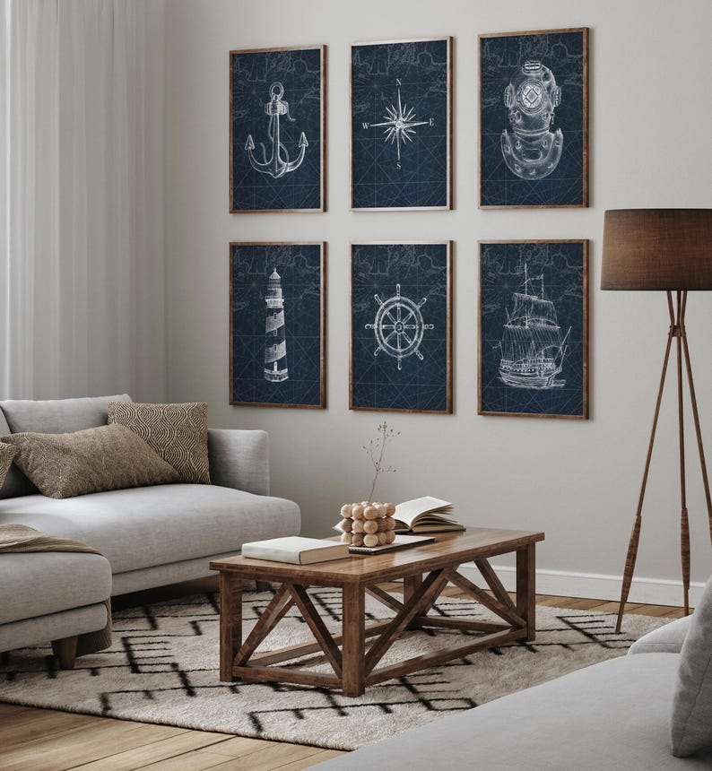 May include: Six framed nautical-themed prints. Each print features a white illustration on a dark blue background, including an anchor, compass rose, diving helmet, lighthouse, ship's wheel, and sailboat. The frames are a warm brown color, and the prints are displayed in a living room setting.