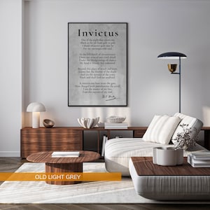 a modern living room with a large framed quote of the poem "Invictus" by William Shakespeare displayed on the wall. The quote is in black text and is surrounded by a wooden frame. The living room has a white sofa, a wooden coffee table, and a lamp on a side table. The overall color scheme of the room is a combination of white and brown, with a touch of black.