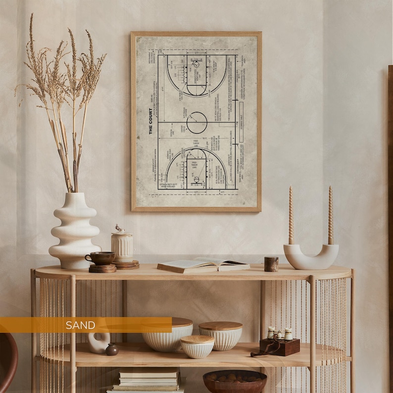 Op de afbeelding: Een ingelijste basketbalveld blauwdruk print in een licht houten frame. De print is in zwart en wit, met gedetailleerde lijnen en tekst. De print wordt weergegeven op een licht houten console met decoratieve items.