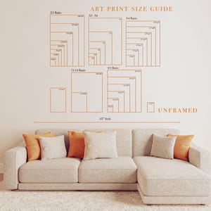 The image is a wall decal that provides an art print size guide for different print sizes, including 23, 23/2, 11/14, 4/5, and unframed. The guide is displayed above a beige sectional sofa with orange throw pillows.