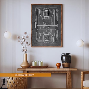 Op de afbeelding: Een ingelijste print van een basketbalveld diagram in wit op een donkergrijze achtergrond. De print is gelabeld "THE COURT" en wordt weergegeven boven een houten console met decoratieve items. De tekst "OLD DARK GREY" staat onderaan.