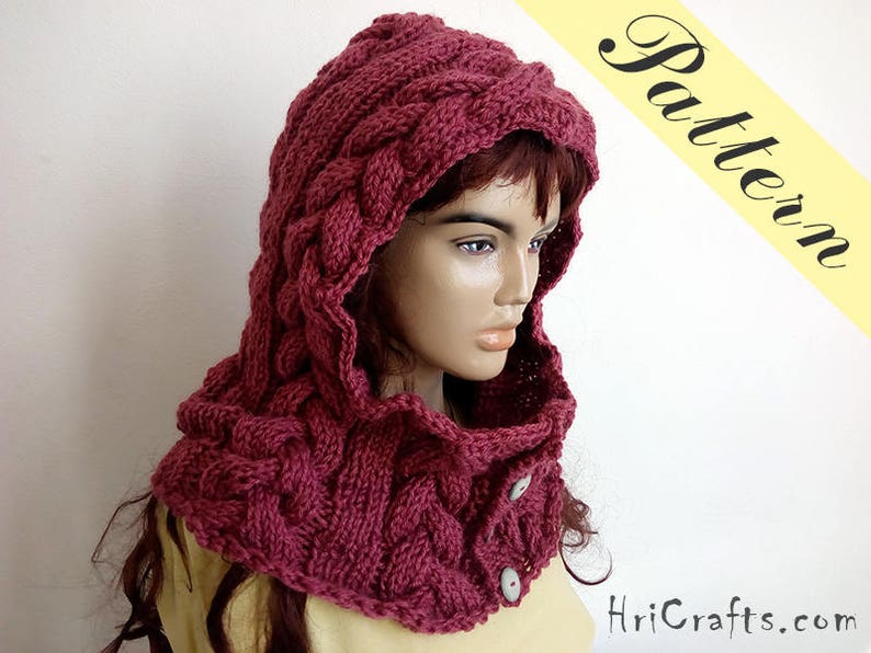 May include: A burgundy knitted hooded cowl with a cable knit pattern and two buttons. The cowl is worn by a person with long brown hair.
