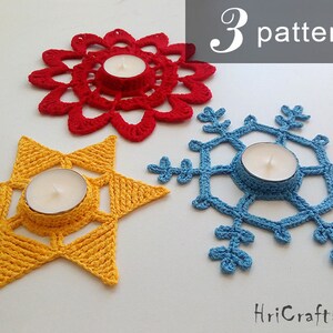 May include: Three crocheted candle holders in the shapes of a star, snowflake, and flower. The star is yellow, the snowflake is blue, and the flower is red. The candle holders are all made with a delicate crochet pattern.