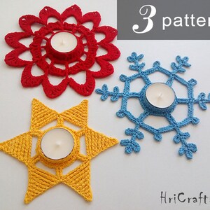 May include: Three crocheted candle holders in the shapes of a flower, snowflake, and star. The flower is red, the snowflake is blue, and the star is yellow. Each holder has a small tea light candle in the center.