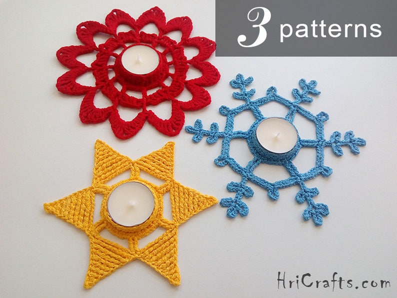 May include: Three crocheted candle holders in the shapes of a flower, snowflake, and star. The flower is red, the snowflake is blue, and the star is yellow. Each holder has a small tea light candle in the center.