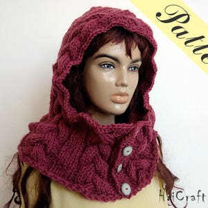 May include: A burgundy knitted cowl with a hood and button closures. The cowl is made of a soft, chunky yarn and has a cable knit pattern.