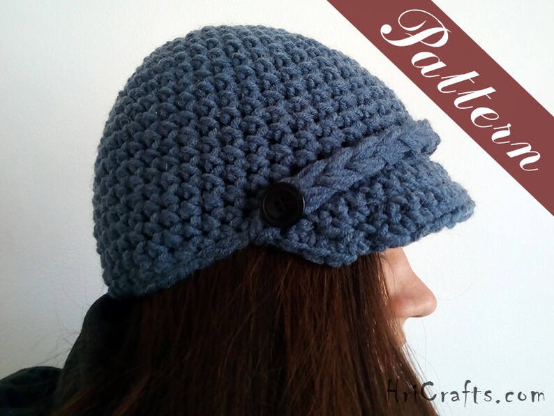 May include: A blue crocheted hat with a brim and a button detail. The hat is worn by a person with long brown hair.