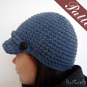 May include: A blue crocheted hat with a brim and a button on the side. The hat is worn by a person with long dark hair.