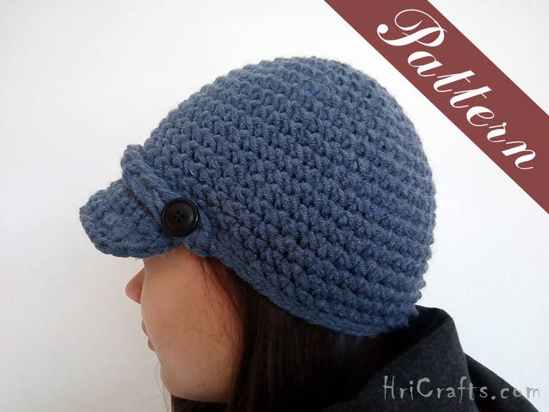 May include: A blue crocheted hat with a brim and a button on the side. The hat is worn by a person with long dark hair.