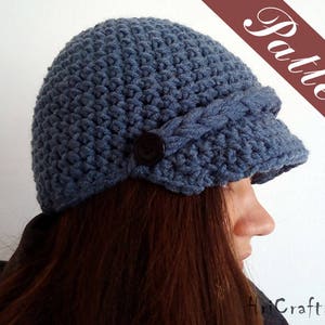 May include: A blue crocheted hat with a wide brim and a button detail. The hat is worn by a person with long brown hair.