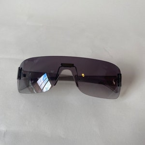 May include: A pair of black sunglasses with a rimless, wraparound design and dark gray lenses.