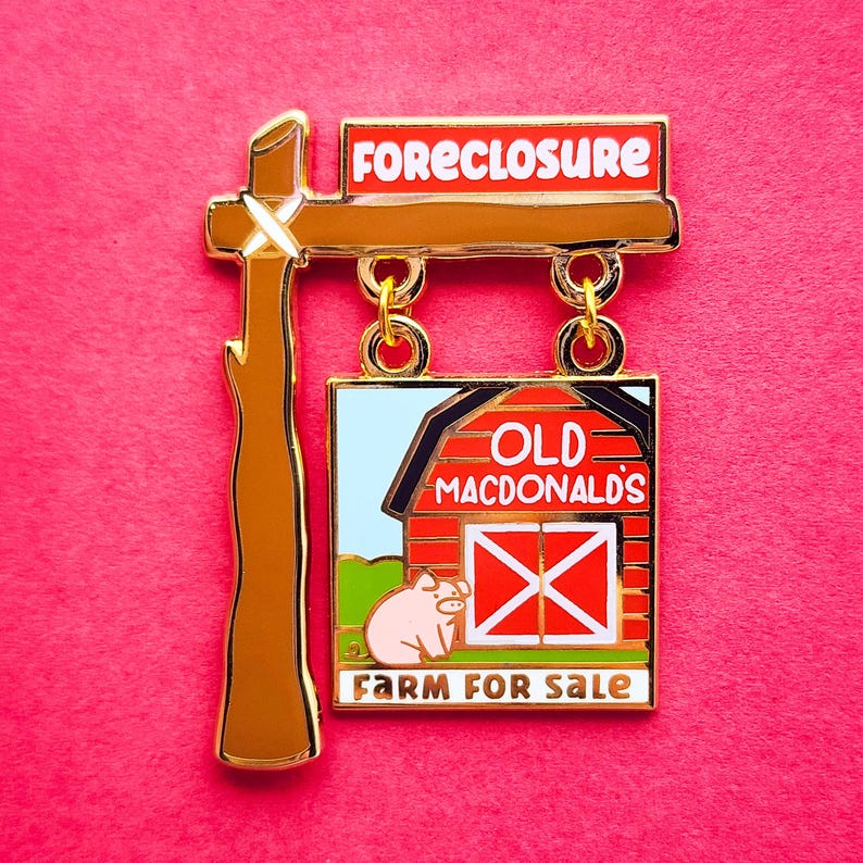May include: A novelty pin with a farm theme. The pin features a sign that reads "FORECLOSURE" above a sign that reads "OLD MACDONALD'S FARM FOR SALE". The pin has a brown post and gold accents, with a pink pig and red barn.