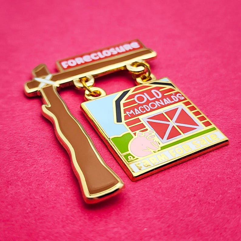 May include: A gold-toned enamel pin with a brown gavel and a sign that reads "FORECLOSURE." Below, a rectangular sign depicts a barn with the words "OLD MACDONALD'S FARM FOR SALE" and a pig.