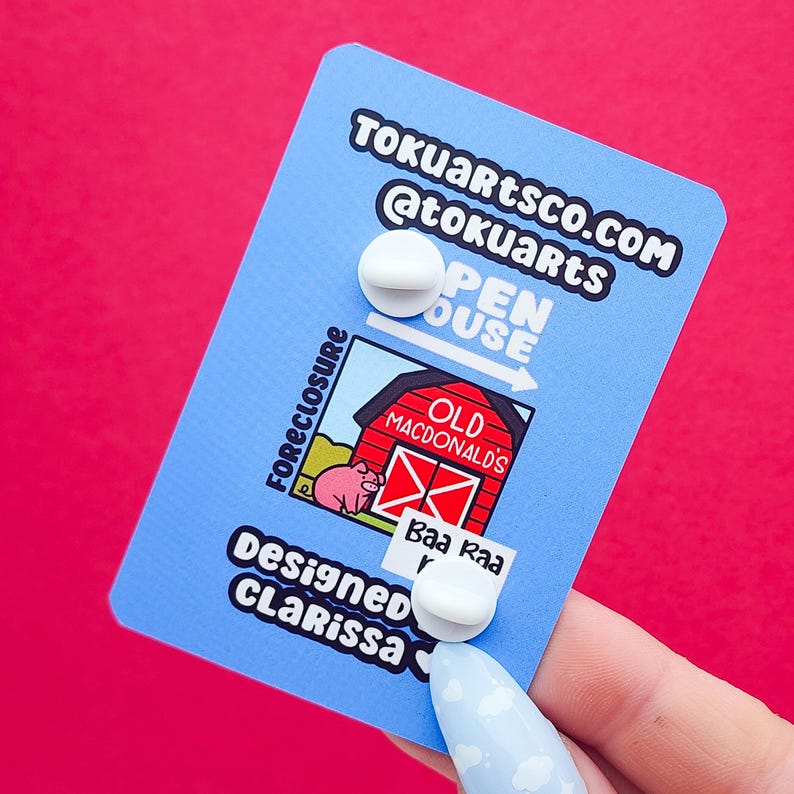 May include: A blue card with white text and two white pin backs. The card features a cartoon barn with a pig and the text "Old MacDonald's". The card also has the text "Foreclosure", "Open House", and "Designed CLarissa".