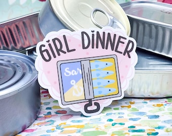 Può includere: Un adesivo rosa e bianco con il testo "Girl Dinner" e un'illustrazione di cartone animato di una scatoletta di sardine. La scatoletta è aperta e mostra quattro sardine all'interno.