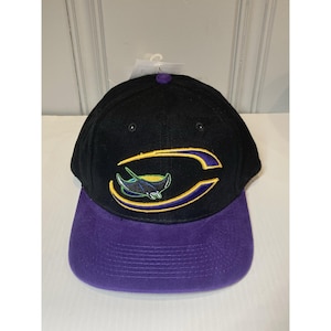 Peut inclure: Casquette de baseball noire avec une visière violette. Le chapeau présente un logo brodé d'une raie manta à l'intérieur d'une lettre "C" stylisée jaune et violette. Le chapeau a un bouton sur le dessus et une étiquette attachée.