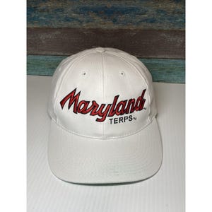 Puede incluir: Gorra de béisbol blanca con la palabra "Maryland" bordada en rojo, con "TERPS™" debajo. La gorra tiene una visera curva y un botón en la parte superior.