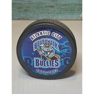 Puede incluir: Disco de hockey negro con el logotipo de los Atlantic City Boardwalk Bullies. El logotipo incluye una mascota de bulldog con un palo de hockey, el nombre del equipo y los años 2002-2003. El disco es de tamaño estándar.