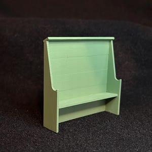 May include: A miniature, light green wooden shelf with a back panel and a small shelf. The shelf is painted in a solid, muted green color. The design is simple and appears to be handmade.