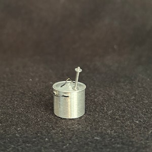 May include: A small silver pot with a handle and a lid. The pot has a small metal stirring rod attached to the lid.