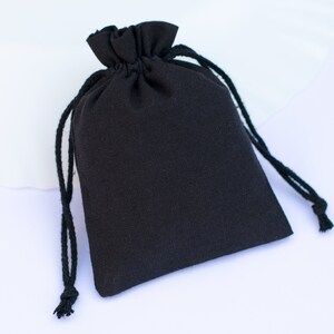 May include: A black drawstring bag with a black cord. The bag is made of a soft, textured fabric.
